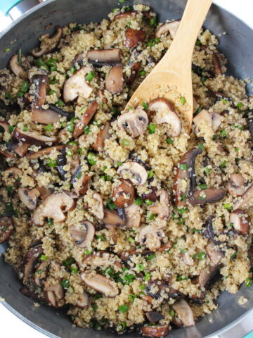 Asian-style quinoa with mushrooms cooking in a pan with wooden spoon