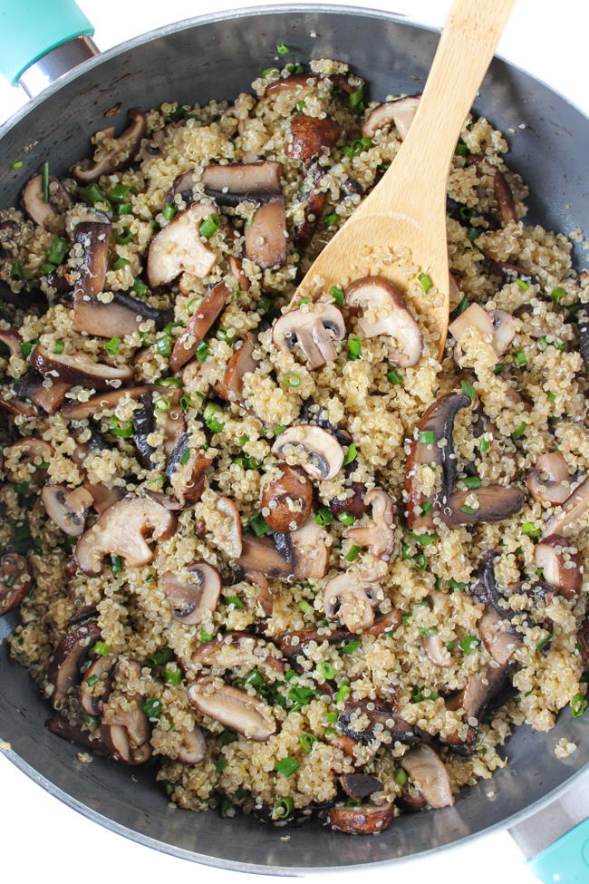 Asian-style quinoa with mushrooms cooking in a pan with wooden spoon