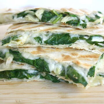 Stacked vegan spinach artichoke quesadillas on a wooden cutting board