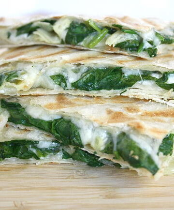 Stacked vegan spinach artichoke quesadillas on a wooden cutting board