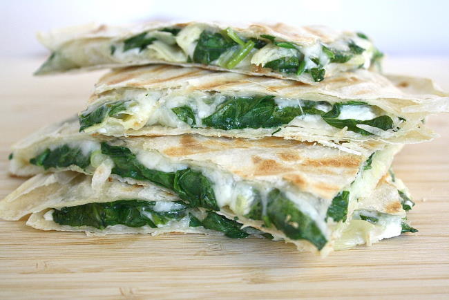 Stacked vegan spinach artichoke quesadillas on a wooden cutting board