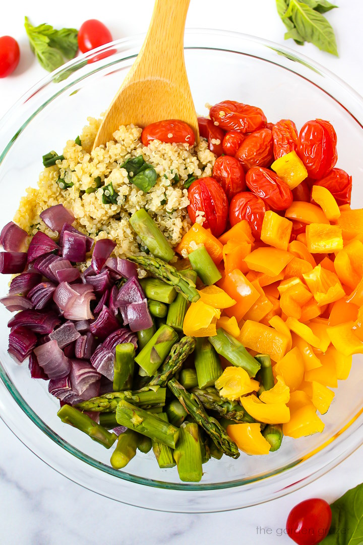 Overhead view of preparing quinoa with roasted vegetables in a large bowl before mixing together