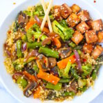 Quinoa vegetable stir fry with tofu in a white serving bowl with chopsticks