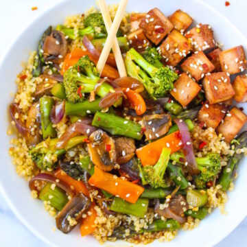 Quinoa vegetable stir fry with tofu in a white serving bowl with chopsticks