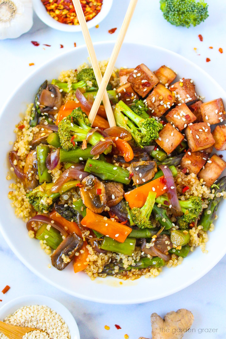 Quinoa vegetable stir fry with tofu in a white serving bowl with chopsticks