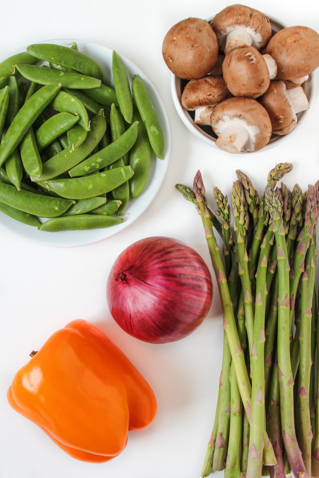 Raw peas, mushrooms, onion, bell pepper, and asparagus on a white table