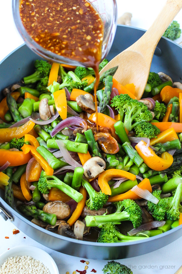 Stir fry sauce being poured over cooked vegetables in a large skillet