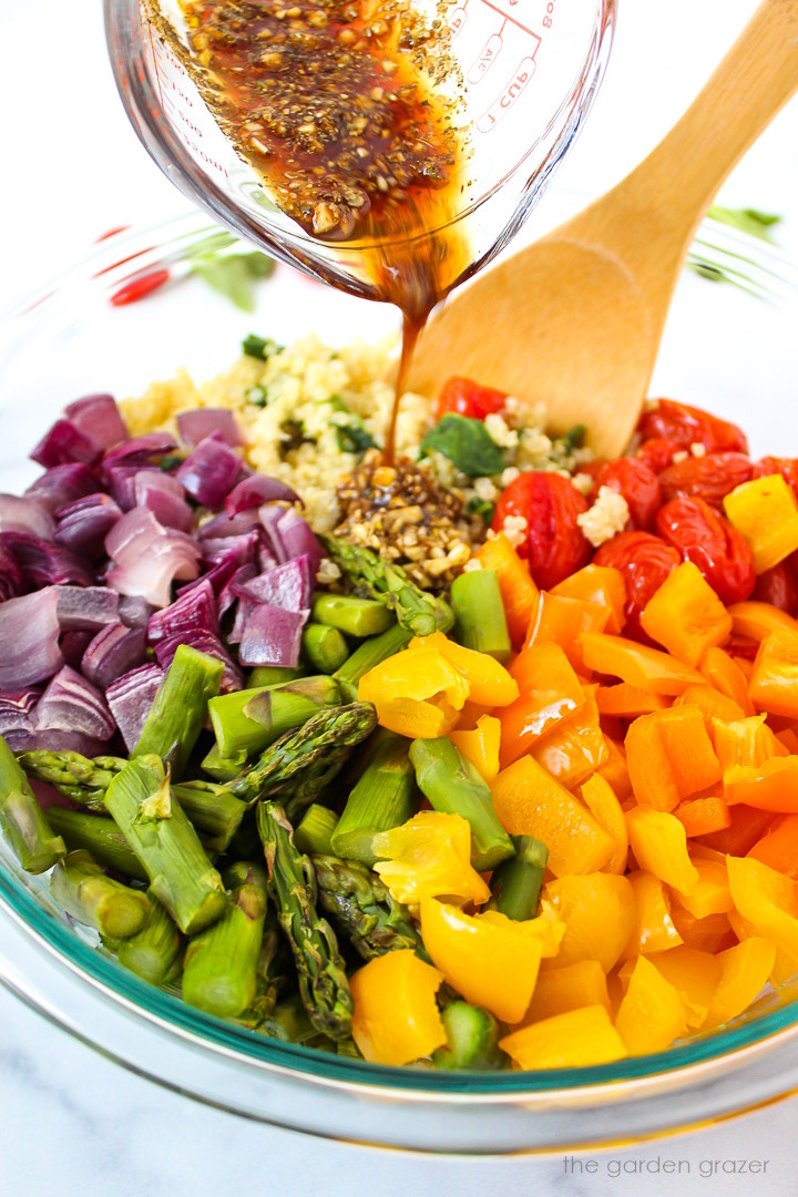 Garlic balsamic dressing being poured over quinoa with roasted vegetables in a large mixing bowl