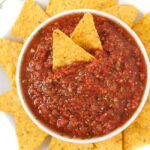Small white bowl of salsa with yellow tortilla chips around it