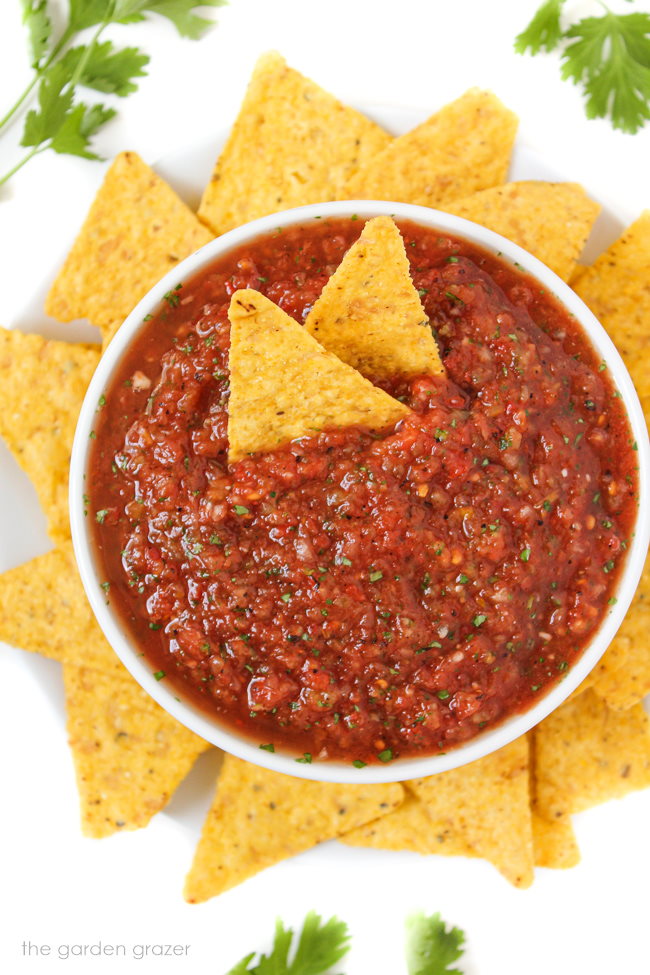 Small white bowl of salsa with yellow tortilla chips around it