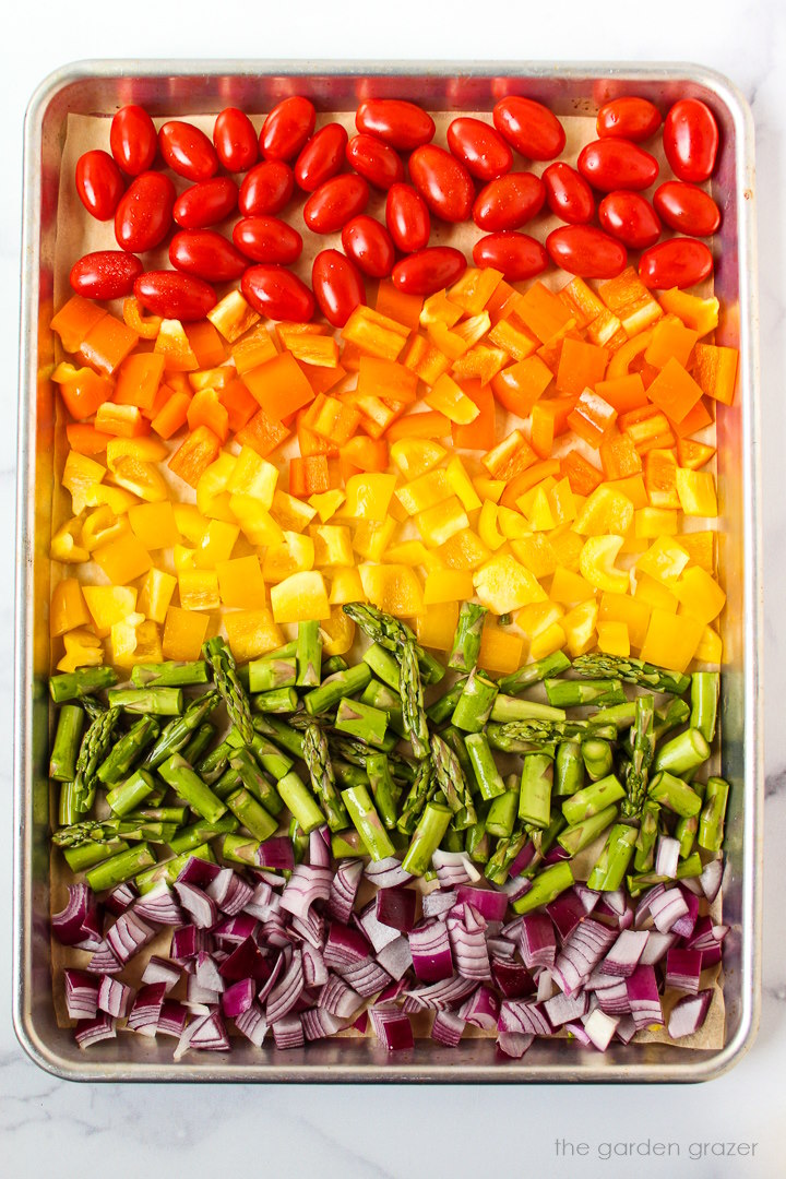 Overhead view of a sheet pan with rainbow chopped veggies lined up before roasting