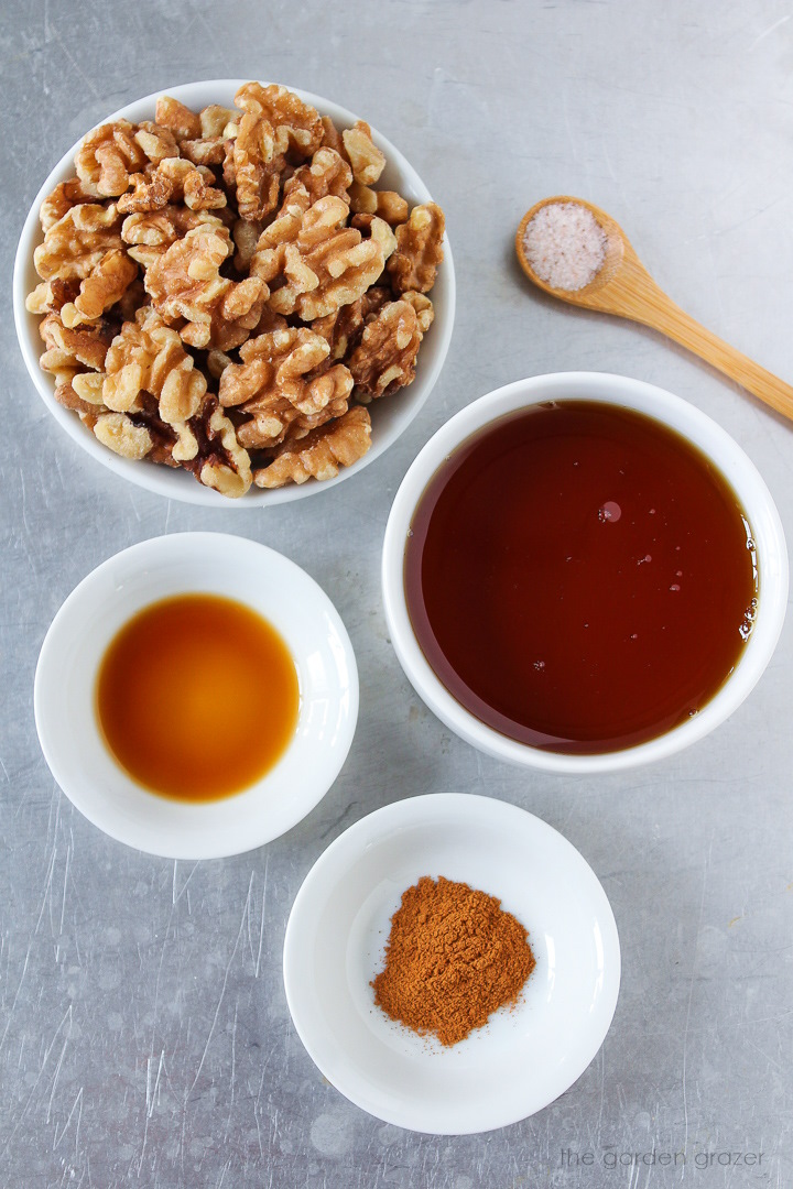 Walnuts, syrup, vanilla extract, ground cinnamon, and salt ingredients laid out on a metal tray