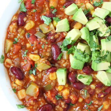 Vegan bulgur vegetable chili in a white bowl with avocado