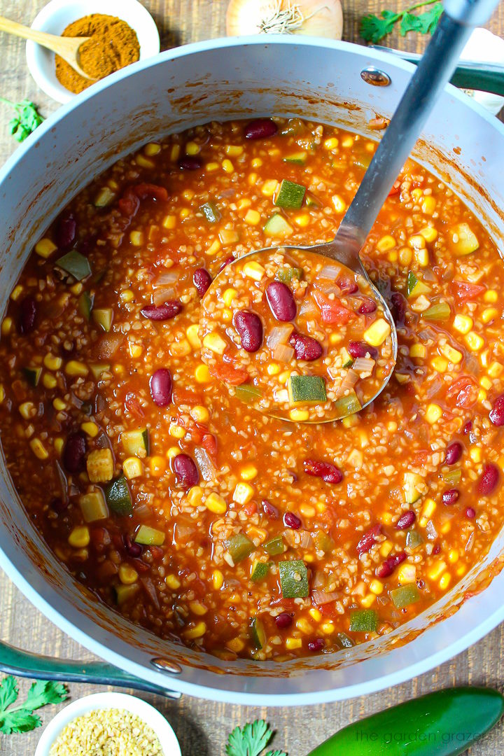 A soup ladle lifting up bulgur chili cooking in a large pot