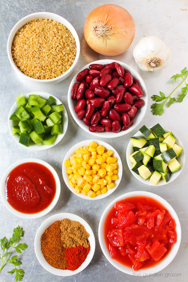 Kidney beans, onion, garlic, green bell pepper, zucchini, sweet corn, tomatoes, and spice ingredients laid out on a metal tray
