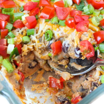 A spoon scooping out refried bean dip in a glass baking dish