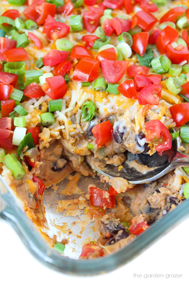 A spoon scooping out refried bean dip in a glass baking dish