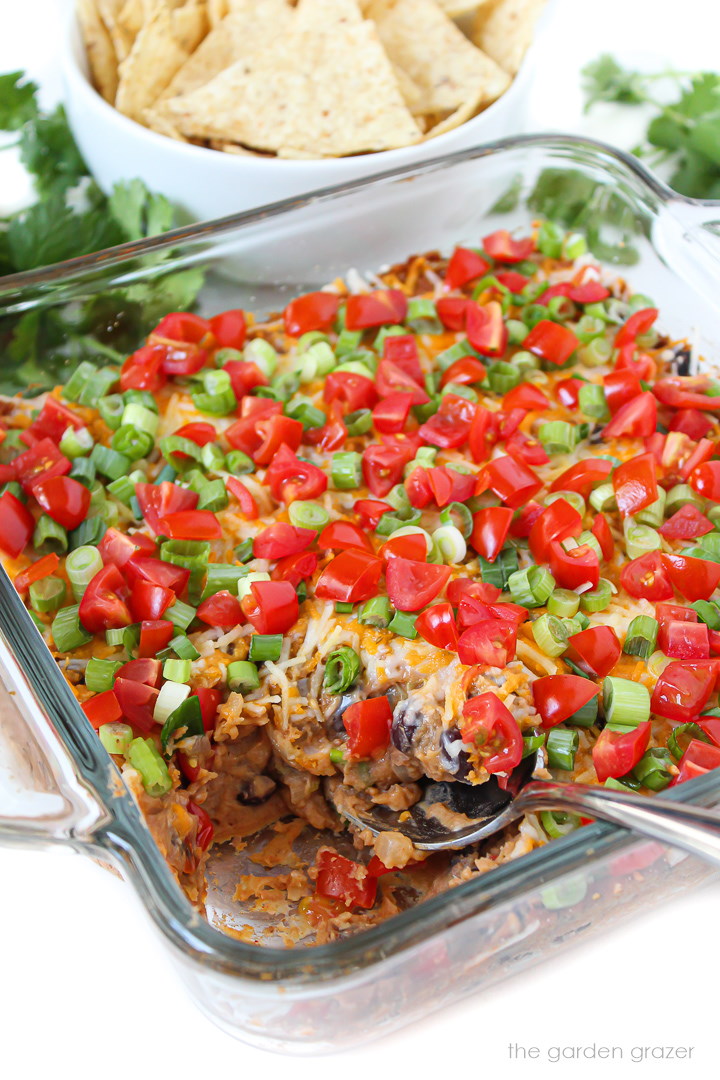 Glass baking dish with bean dip topped with tomatoes and green onions