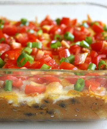 Vegan bean dip in a glass dish topped with tomatoes and green onions