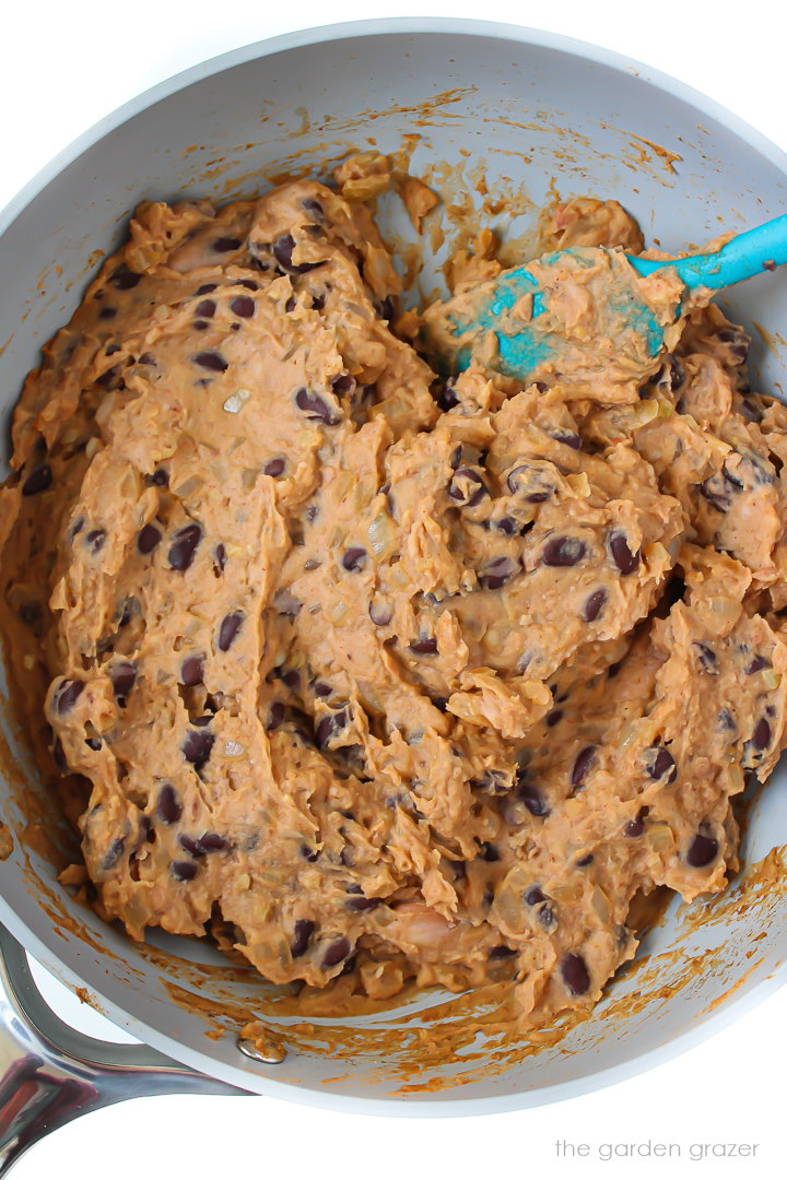 Preparing the bean dip in a skillet with blue spatula