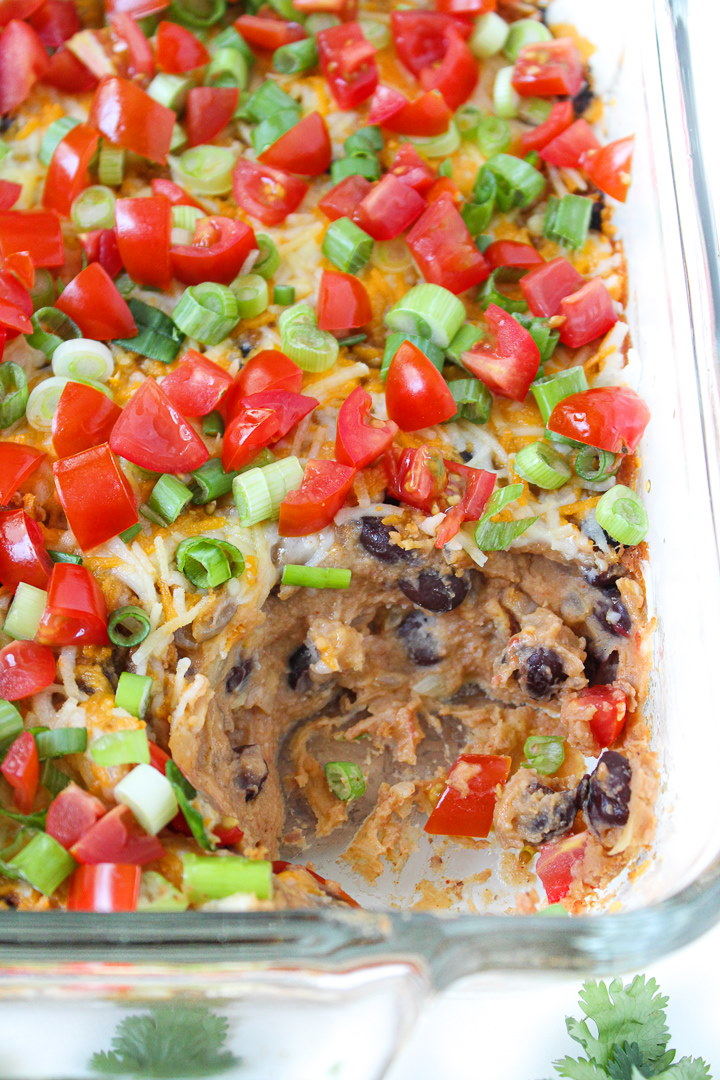 Vegan bean dip in a glass dish topped with tomatoes and green onions