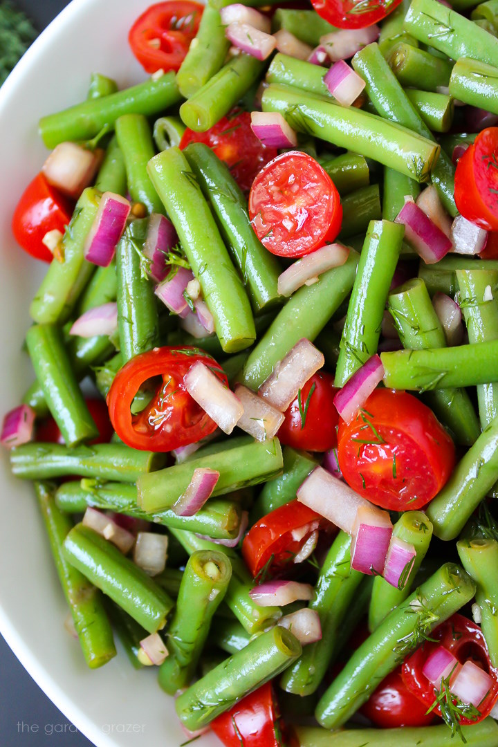 Close up view of balsamic green beans salad on a white plate with onion and tomato