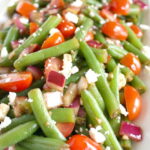 Balsamic green bean salad with onion and tomato on a white plate