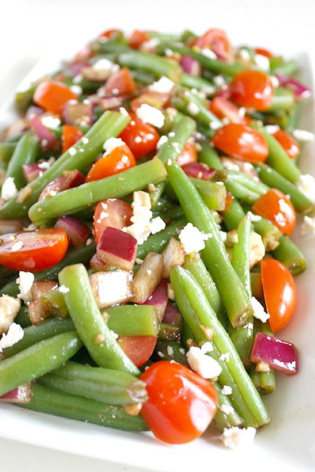Balsamic green bean salad with onion and tomato on a white plate