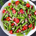Overhead view of balsamic green beans salad on a white plate with tomato, onion, and dill