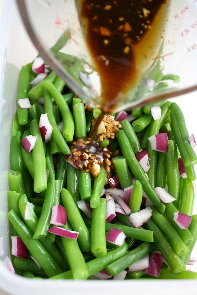 Dressing being poured over green beans for salad preparation