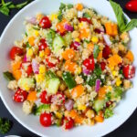 Overhead view of quinoa vegetable salad in a white bowl with fresh basil