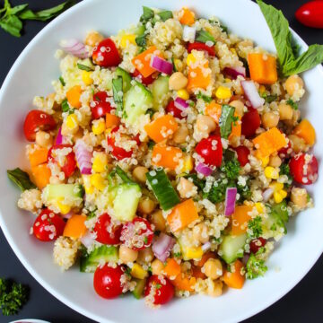 Overhead view of quinoa vegetable salad in a white bowl with fresh basil