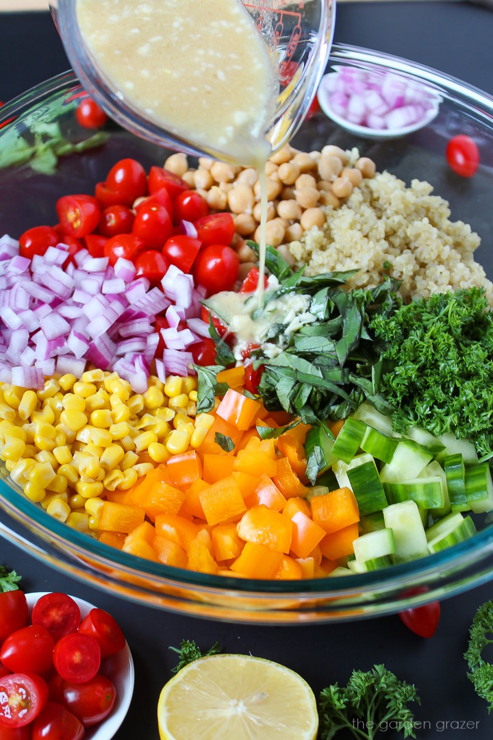 Lemon garlic dressing being poured over a quinoa vegetable salad in a large glass mixing bowl