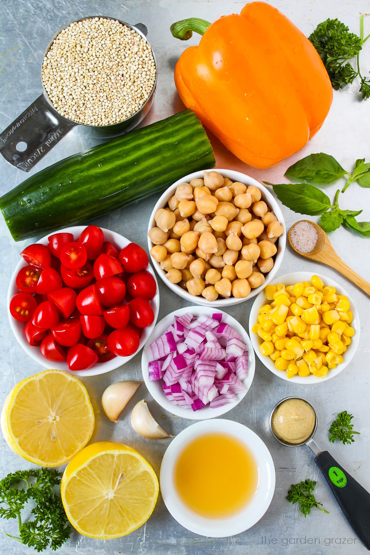 Bell pepper, cucumber, red onion, sweet corn, tomato, lemon, basil, and vinegar ingredients laid out on a metal tray