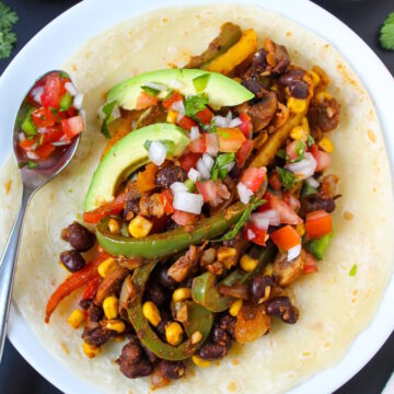 Corn and black bean fajitas served on a white plate with fresh salsa and avocado
