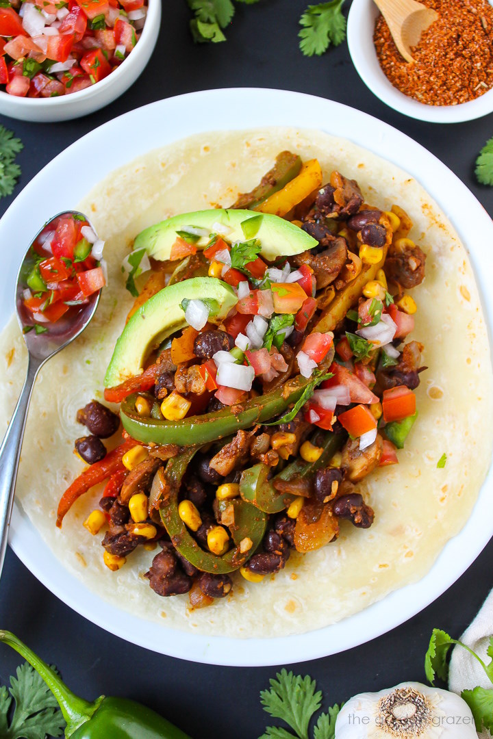 Corn and black bean fajitas served on a white plate with fresh salsa and avocado
