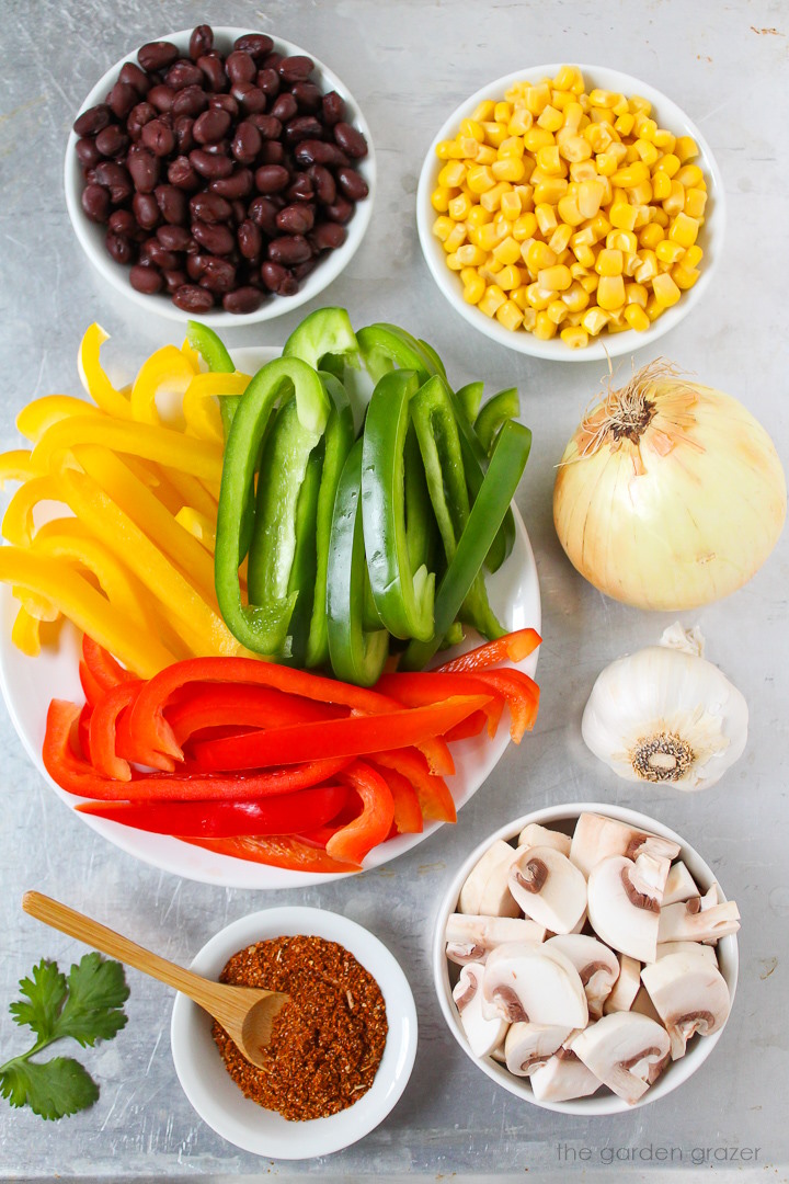 Sliced bell peppers, sweet corn, onion, garlic, mushrooms, and taco seasoning ingredients laid out on a metal tray