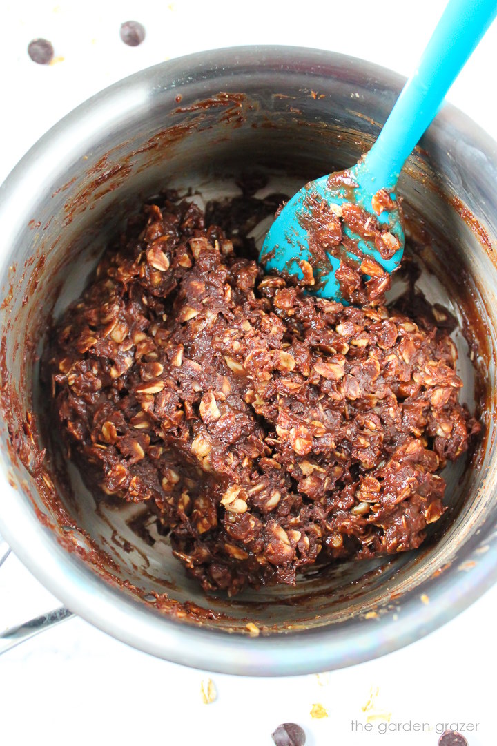 Overhead view of chocolate oat balls mixture heating in a small pan with spatula