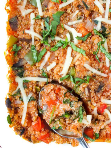 Close up view of vegan pizza quinoa casserole in a glass baking dish with serving spoon