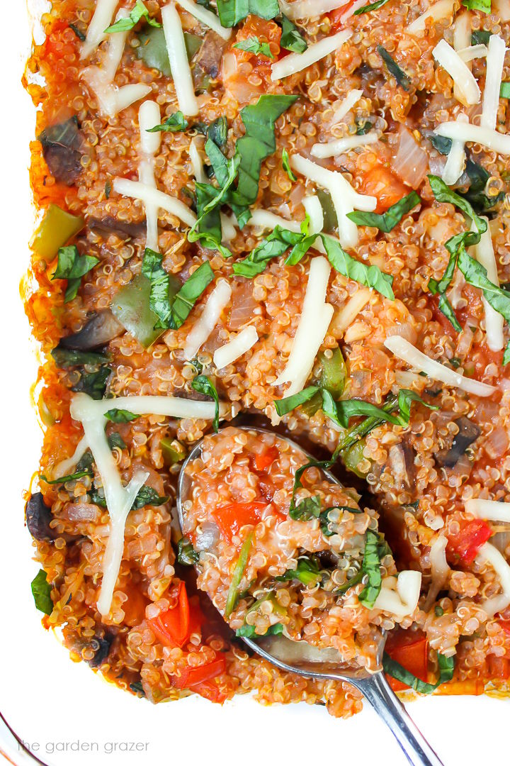 Close up view of vegan pizza quinoa casserole in a glass baking dish with serving spoon