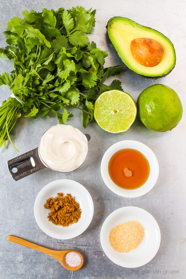Fresh herbs, avocado, dairy-free yogurt, fresh lime, garlic powder, cumin, and salt ingredients laid out on a metal tray