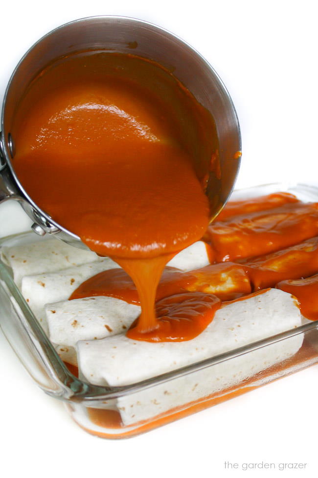 Homemade enchilada sauce being poured over a pan of enchiladas