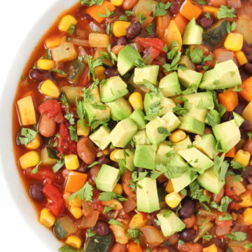 Vegan summer vegetable chili in a bowl topped with avocado and cilantro