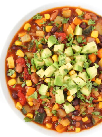 Vegan summer vegetable chili in a bowl topped with avocado and cilantro