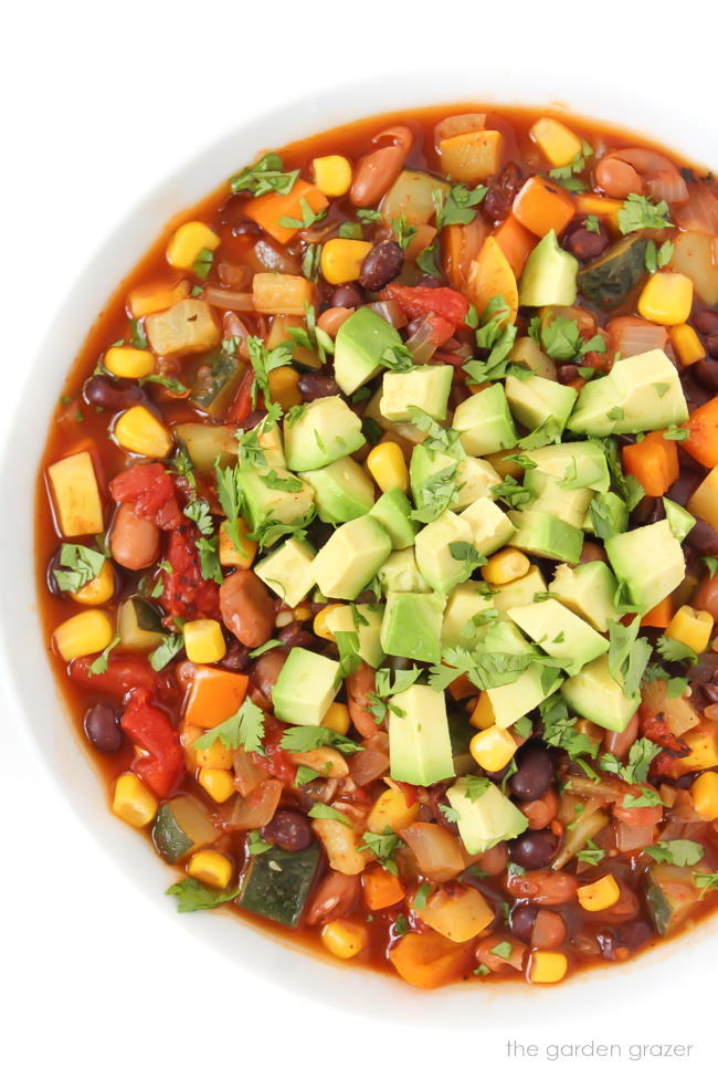 Vegan summer vegetable chili in a bowl topped with avocado and cilantro