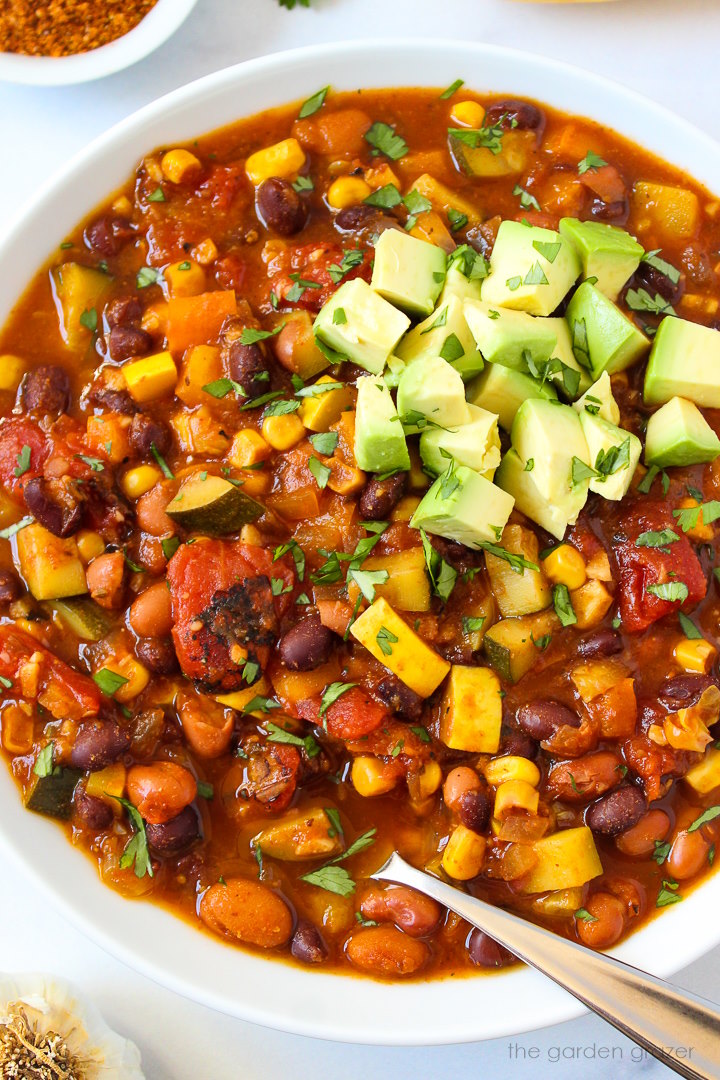 Close up view of summer vegetable chili in a white serving bowl with spoon
