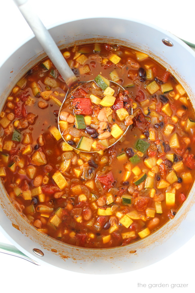 Vegan summer vegetable chili cooking in a large stockpot with ladle