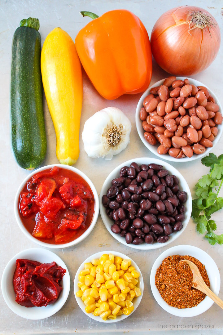 Zucchini, summer squash, tomatoes, onion, bell pepper, corn, beans, and seasoning ingredients laid out on a metal tray