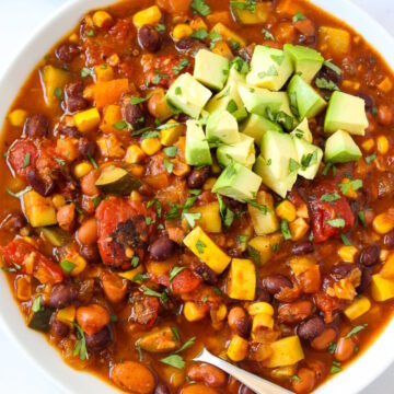 Vegan summer vegetable chili in a white serving bowl topped with avocado and fresh cilantro