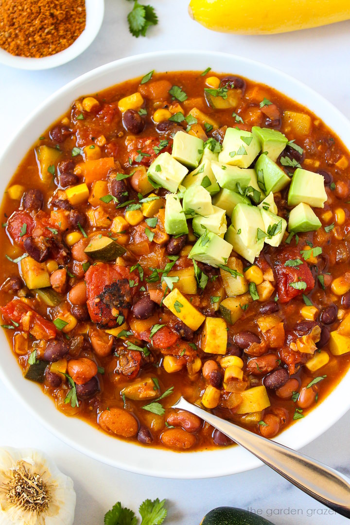Vegan summer vegetable chili in a white serving bowl topped with avocado and fresh cilantro
